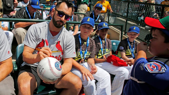 St. Louis Cardinals' Matt Carpenter, left, signs a giant baseball while he sits with members of the Little League team from Australia at Lamade Field.