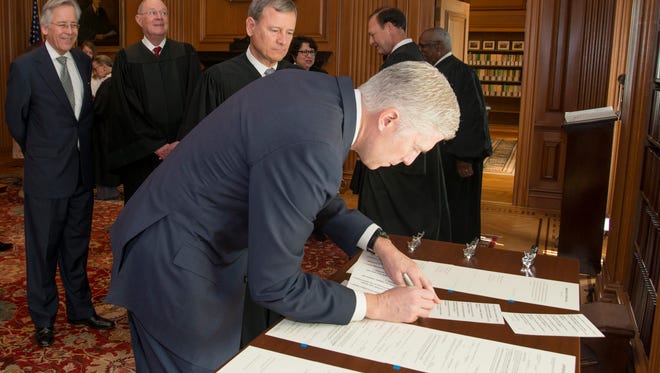 In this photo provided by the Supreme Court's Public Information Office, Chief Justice John Roberts and fellow justices watch as Neil Gorsuch signs the constitutional oath after a private ceremony on April 10, 2017, at the Supreme Court.