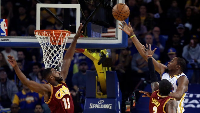 Kevin Durant lays up a shot against Cleveland Cavaliers' Tristan Thompson and Kyrie Irving.